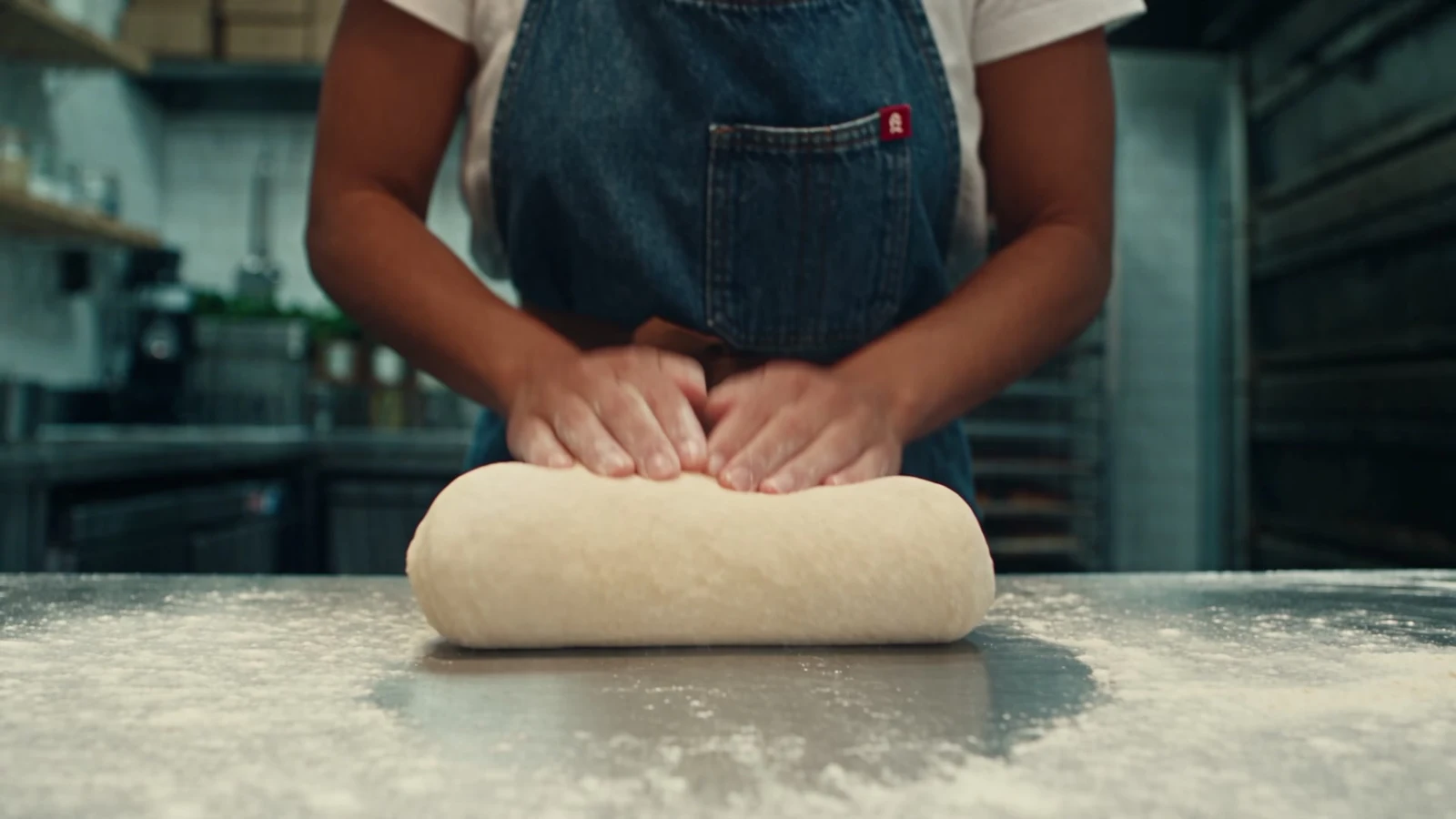 Hands kneading dough on a floured steel counter, a frame from the AI film